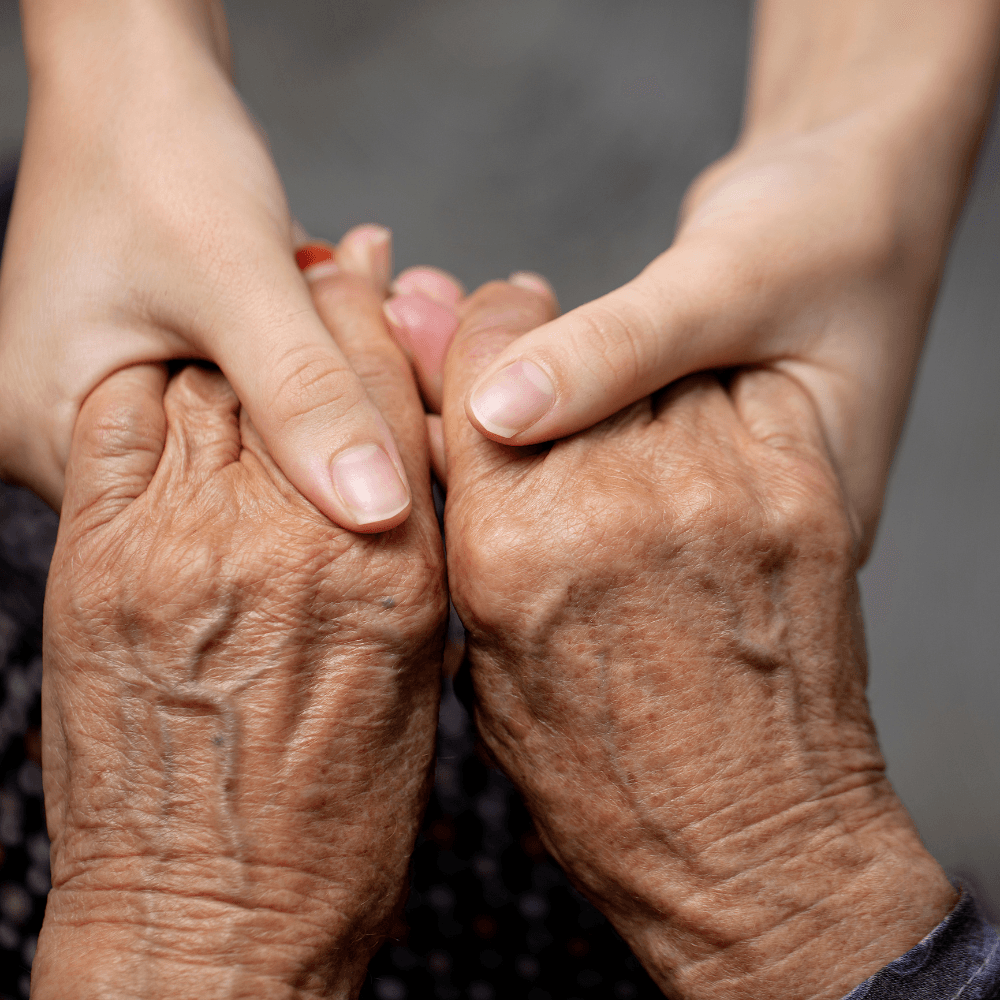 A younger person's hands gently holding an older person's hands