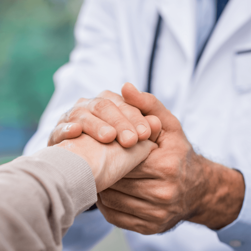 A caregiver in a white coat holding an older person's hands