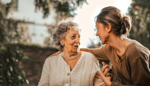 A caregiver and an older woman laughing together outdoors