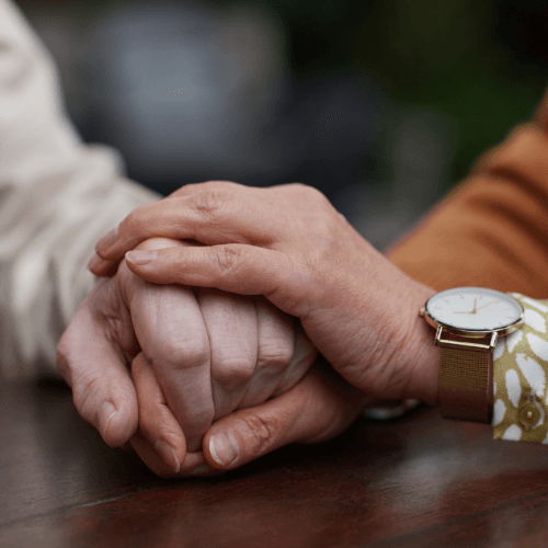 A caregiver's hands resting reassuringly on an older person's hands